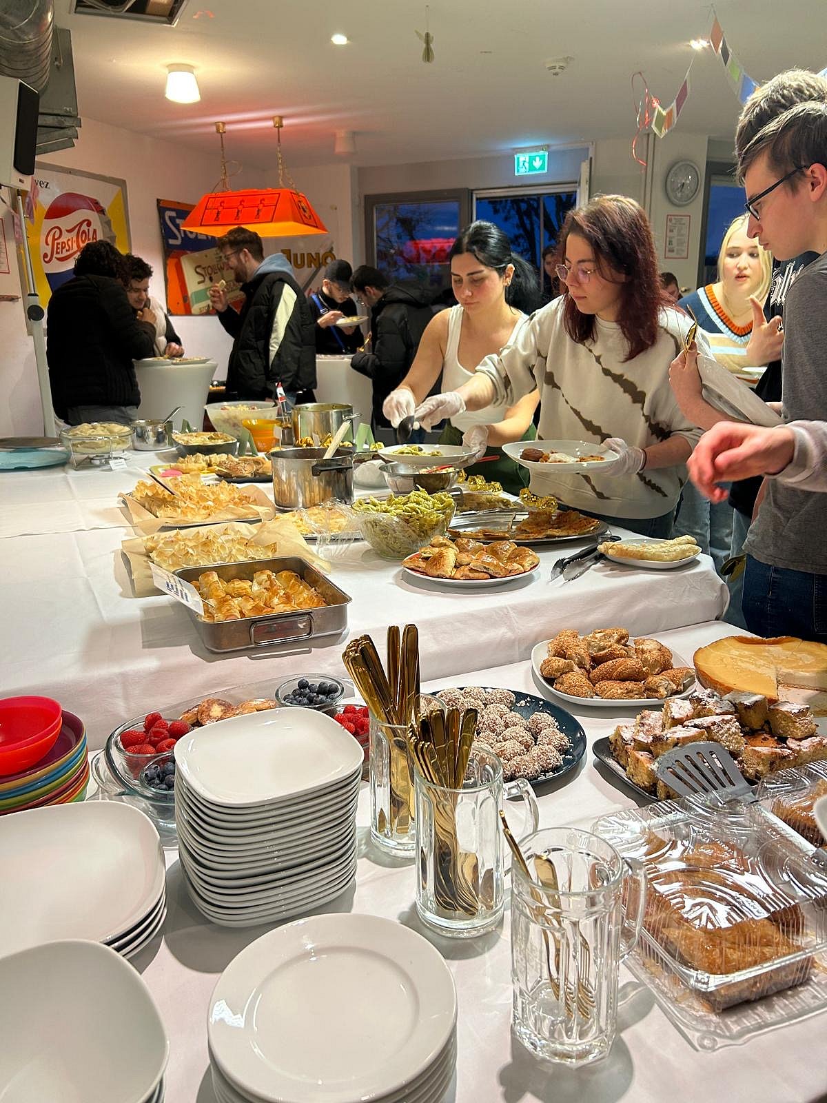Viele Personen an einem Buffet. Teller, Besteck und viele unterschiedliche Gerichte stehen darauf.