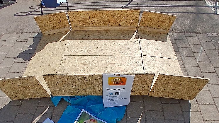 Auf dem Steinboden im Schulhof steht eine Brücke aus Holz mit Begrenzungen an der Seite.