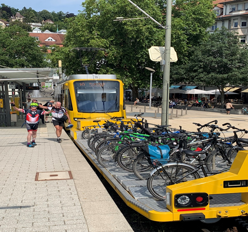 Abgebildet sind Tandems und Fahrräder, die außen am Abteil einer Straßenbahn befestigt sind.