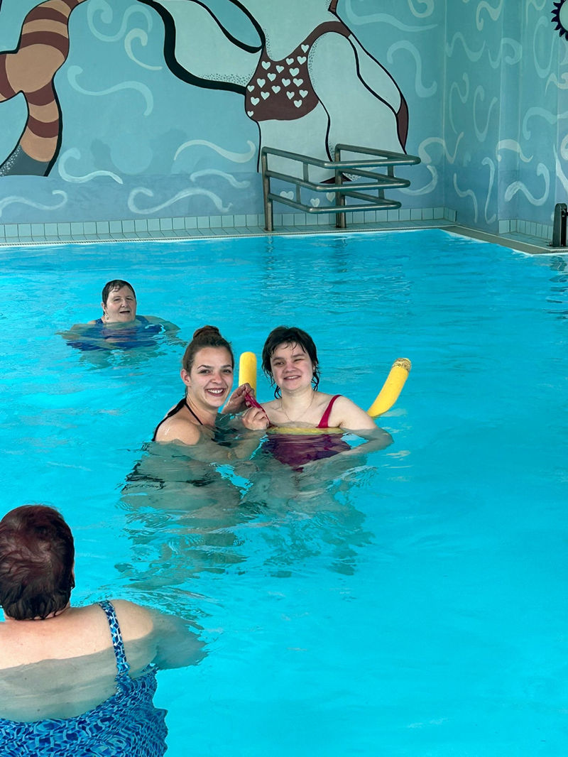 Eine Mitarbeiterin der Nikolauspflege schwimmt gemeinsam mit einer Klientin in einem Schwimmbad